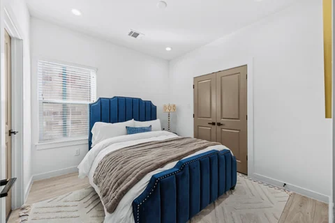 Bedroom with a blue upholstered bed, neutral bedding, and a window
