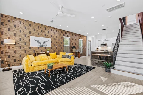 Open living and dining room with a yellow sofa, patterned wall, and staircase