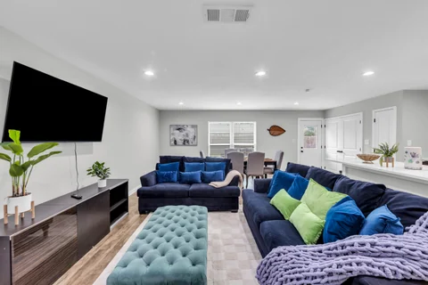 Open living room with blue sofas, colorful cushions, a television, and dining space