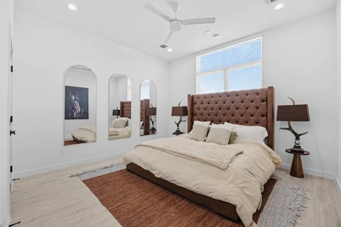Bedroom with a tufted headboard, bedside lamps, and tall mirrors