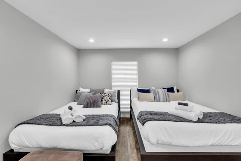 Bedroom with two beds, white bedding, patterned throws, and a window